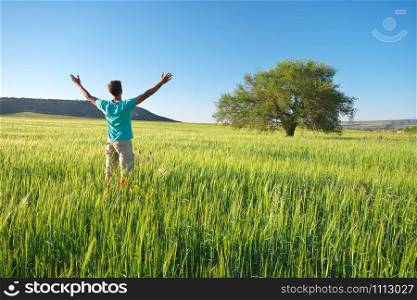 Man in green meadow of wheat and big tree. Emotional scene.
