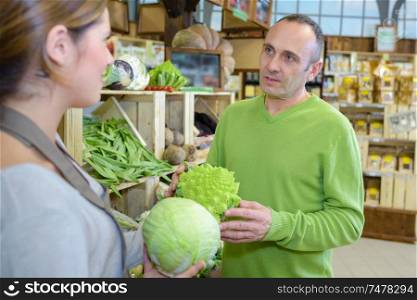 Man in greengrocers asking advice from shop assistant