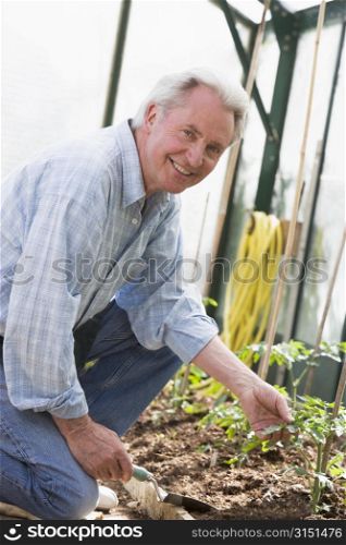 Man in greenhouse holding shovel smiling