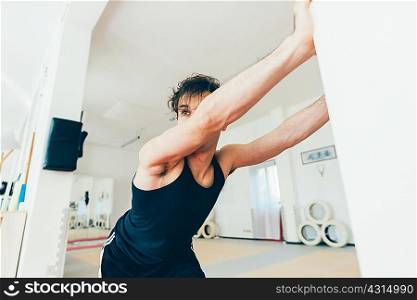 Man in gym leaning against wall stretching