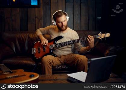 Man in headphones playing guitar listening looking at laptop screen. Online music lesson. Man playing guitar listening looking at laptop