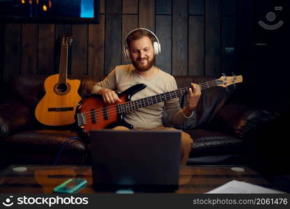 Man in headphones playing guitar listening looking at laptop screen. Online music lesson. Man playing guitar listening looking at laptop