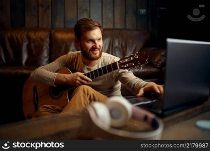 Man in headphones playing guitar listening looking at laptop screen. Online music lessons. Man playing guitar listening looking at laptop