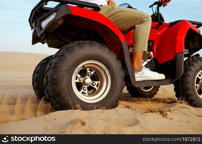 Man in helmet rides on atv, downhill riding in desert sands, action view. Male person on quad bike, sandy race, dune safari in hot sunny day, 4x4 extreme adventure, quad-biking. Man in helmet rides on atv in desert, action view