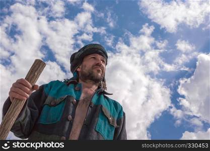 Man in his turban leaning on the stick looks into the distance under a blue sky with beautiful clouds, bottom view.. Man in his turban under a blue cloudy sky