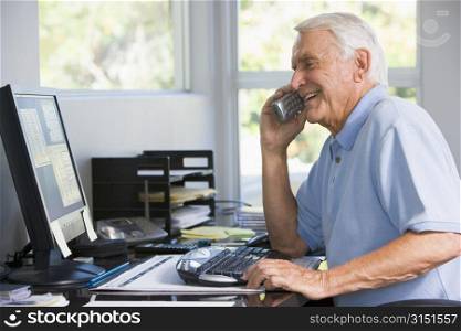 Man in home office on telephone using computer smiling