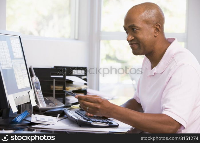 Man in home office using computer holding credit card and smiling