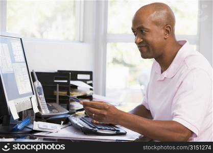 Man in home office using computer holding credit card and smiling