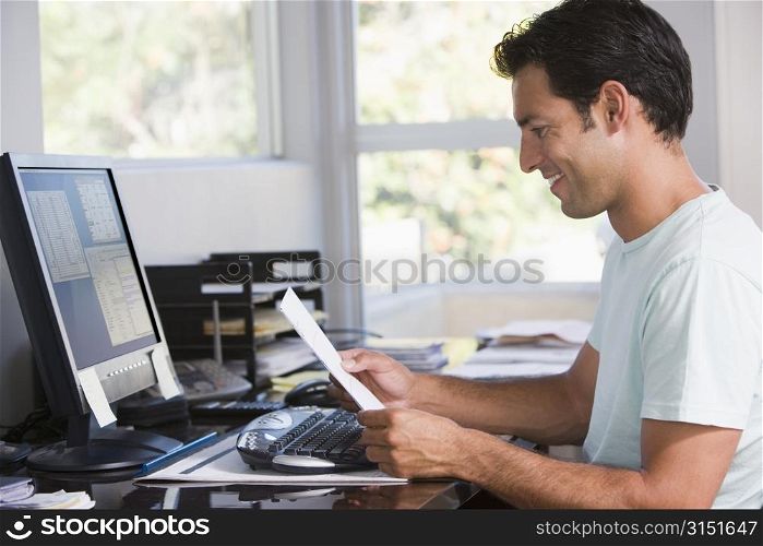 Man in home office using computer holding paperwork and smiling