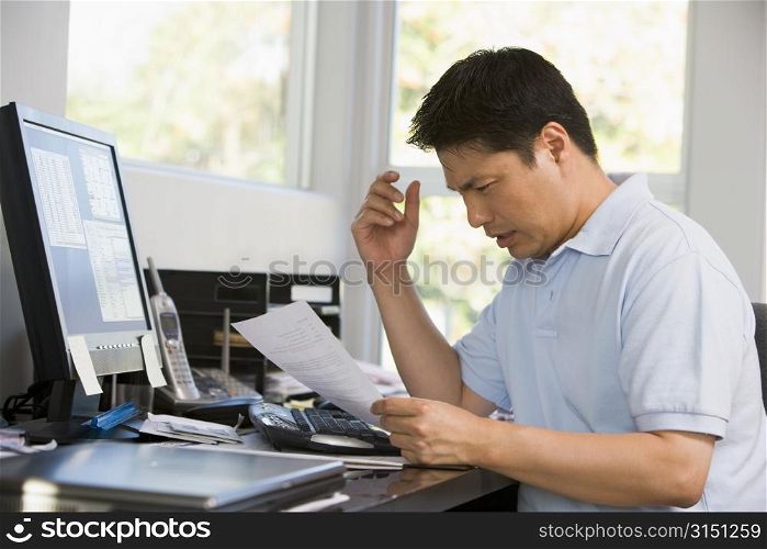Man in home office with computer and paperwork frustrated