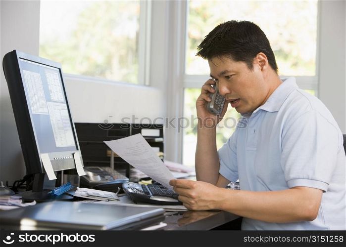 Man in home office with computer and paperwork on telephone