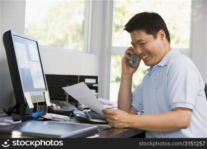 Man in home office with computer and paperwork on telephone smiling