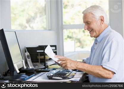 Man in home office with computer and paperwork smiling