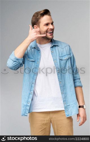 man in jeans shirt making a call me gesture standing over studio grey background.. man in jeans shirt making a call me gesture standing over studio grey background