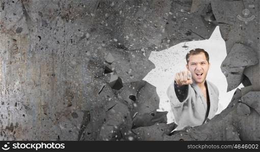 Man in kimono breaking wall. Young determined karate man breaking concrete wall