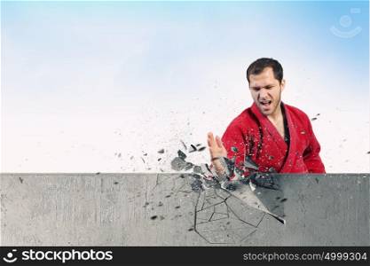Man in kimono breaking wall. Young determined karate man breaking concrete wall