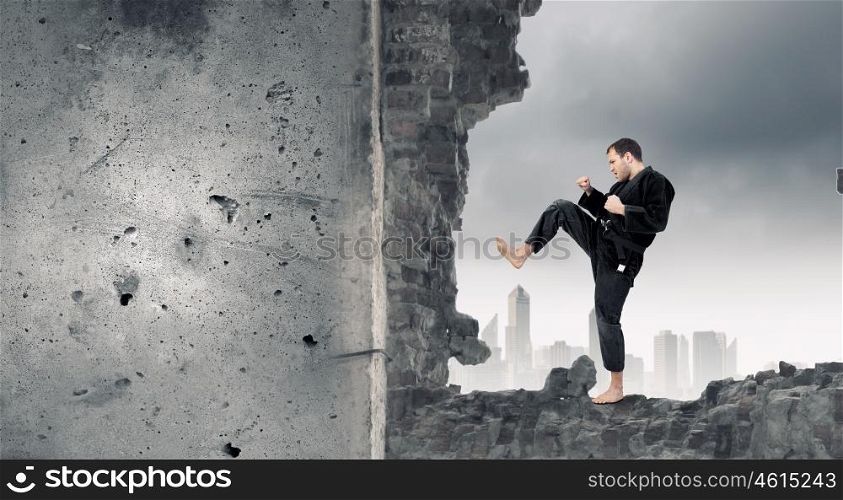 Man in kimono breaking wall. Young determined karate man breaking with leg concrete wall