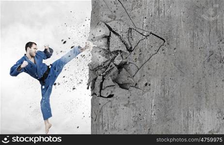 Man in kimono breaking wall. Young determined karate man breaking with leg concrete wall