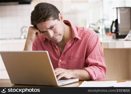 Man in kitchen using laptop frowning