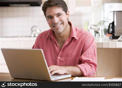Man in kitchen using laptop smiling