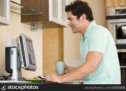 Man in kitchen with coffee using computer and smiling