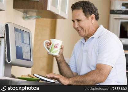 Man in kitchen with computer and coffee smiling