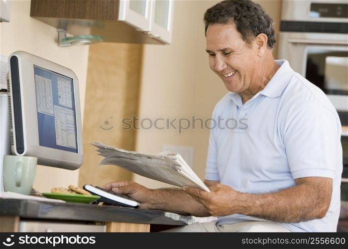 Man in kitchen with computer and newspaper smiling