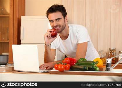 Man in kitchen with laptop and vegetables
