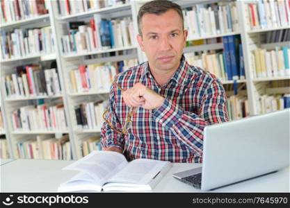 Man in library with book and laptop