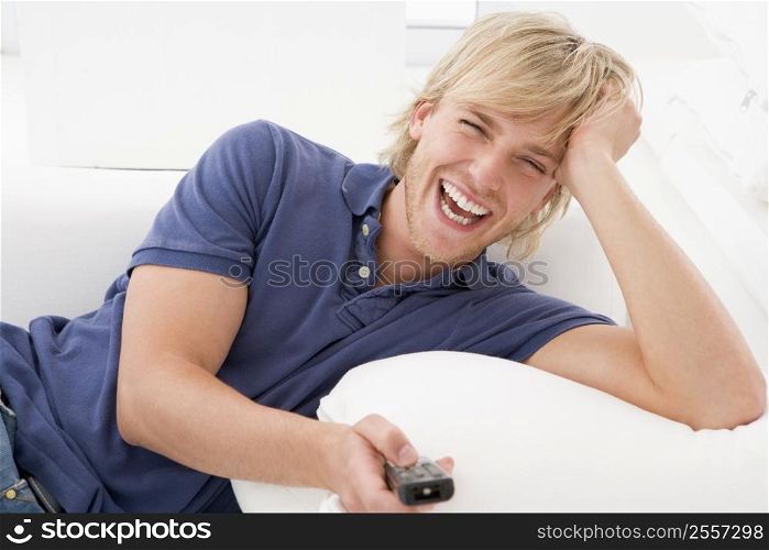 Man in living room holding remote control laughing