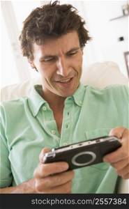Man in living room playing handheld videogame smiling