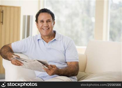 Man in living room reading newspaper smiling