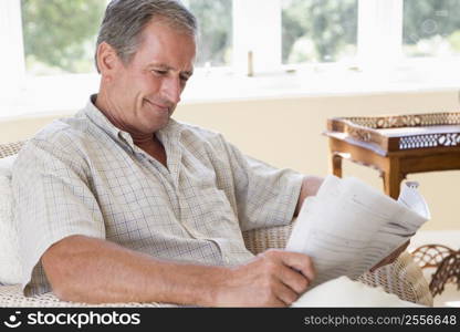 Man in living room reading newspaper smiling