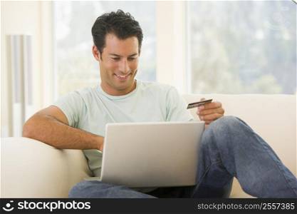 Man in living room using laptop and holding credit card smiling