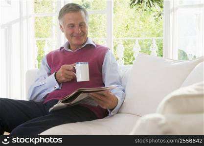 Man in living room with coffee reading newspaper smiling