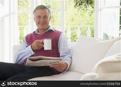 Man in living room with coffee reading newspaper smiling