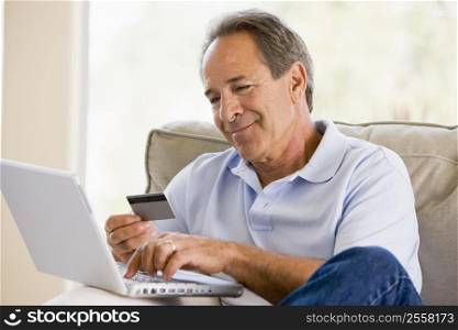 Man in living room with laptop and credit card smiling
