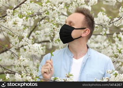 man in mask among flowering trees. man in a medical mask among a blossoming spring garden. Self-isolation and quarantine. cheerful man rejoices in the end of the pandemic and enjoys the spring. man in mask among flowering trees. man in a medical mask among a blossoming spring garden. Self-isolation and quarantine. cheerful man rejoices in the end of the pandemic and enjoys the spring.