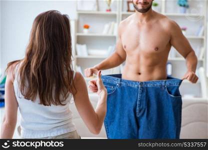 Man in oversized pants in weight loss concept with girlfriend wi. Man in oversized pants in weight loss concept with girlfriend wife