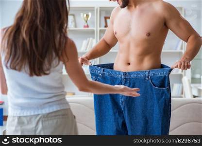 Man in oversized pants in weight loss concept with girlfriend wi. Man in oversized pants in weight loss concept with girlfriend wife
