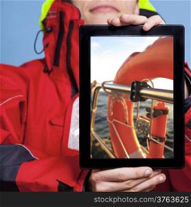 Man in red jacket holding ipad with photo of lifebouy on yacht boat. Sailor showing screen tablet touchpad recommending safety on sailboat. Technology and cruise.