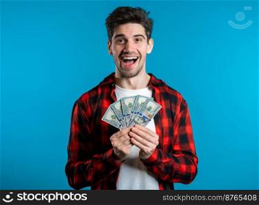 Man in red plaid shirt with surprised happy face holding US currency. Person with money. New dollars in hands on blue studio background. Man in red plaid shirt with surprised happy face holding US currency. Person with money. New dollars in hands on blue studio background .