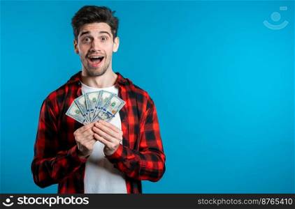 Man in red plaid shirt with surprised happy face holding US currency. Person with money. New dollars in hands on blue studio background. Man in red plaid shirt with surprised happy face holding US currency. Person with money. New dollars in hands on blue studio background .