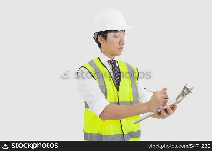 Man in reflector vest and hard hat writing on clipboard in office