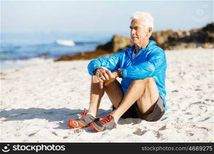 Man in sports wear sitting at the beach. Man in sports wear sitting alone at the beach and having minute of rest