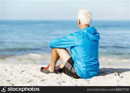 Man in sports wear sitting at the beach. Man in sports wear sitting alone at the beach and having minute of rest