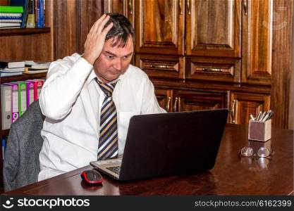 Man in Study with Laptop has his right hand in his hair as he stresses about what he sees on the screen of the computer.