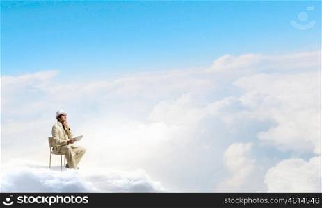 Man in suit and hat use tablet. Young businessman sitting in chair on cloud and using tablet