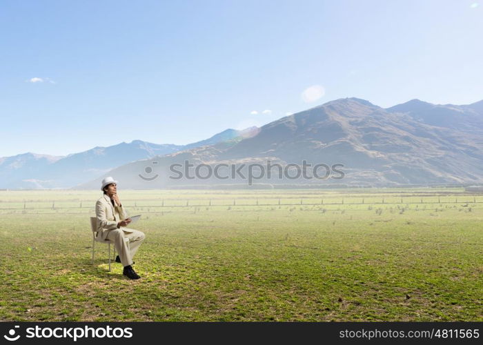 Man in suit and hat use tablet. Young businessman sitting in chair outdoor and using tablet