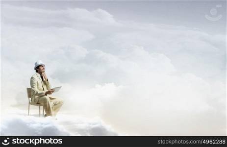Man in suit and hat use tablet. Young businessman sitting in chair on cloud and using tablet